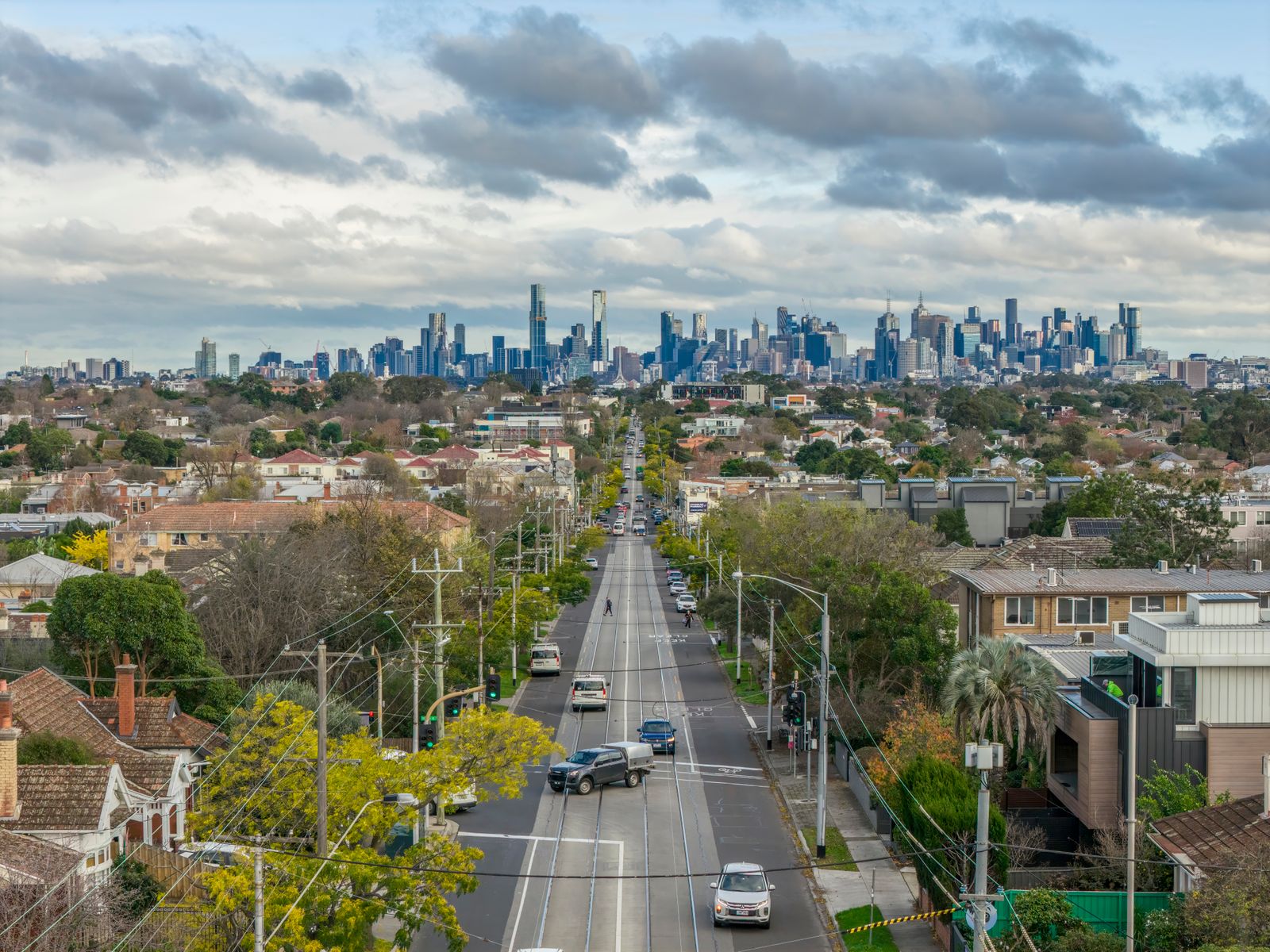 Suburban road lined with trees leading towards a city skyline